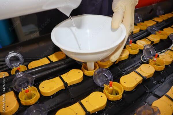watering-forklift-battery A technician adding water to a forklift battery using a funnel