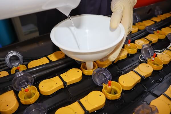 A technician pouring water into a forklift battery cell