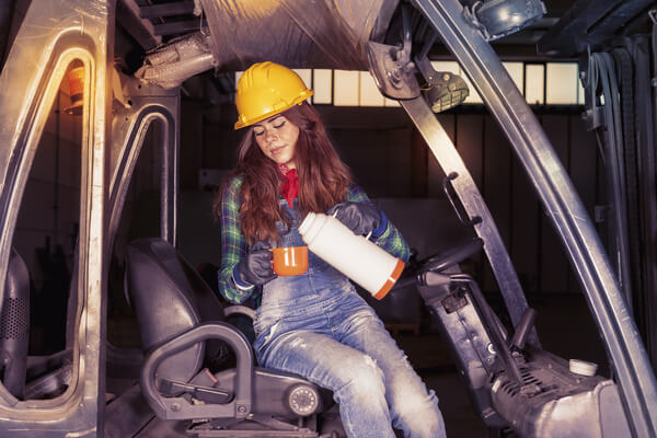 A forklift operator pouring herself a cup of coffee while taking a break